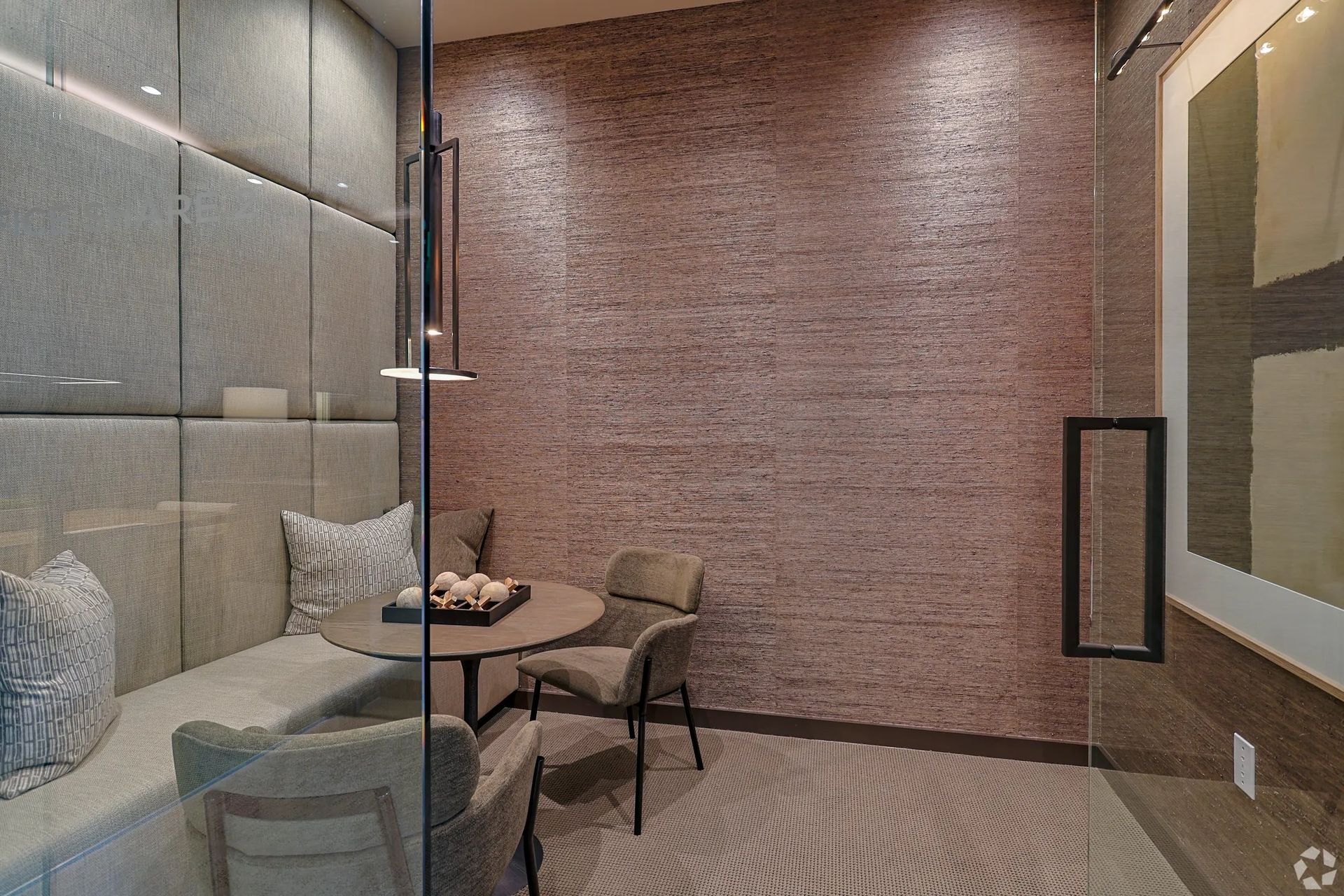 Modern meeting nook with glass wall, round table, chairs, and pink textured accent wall.