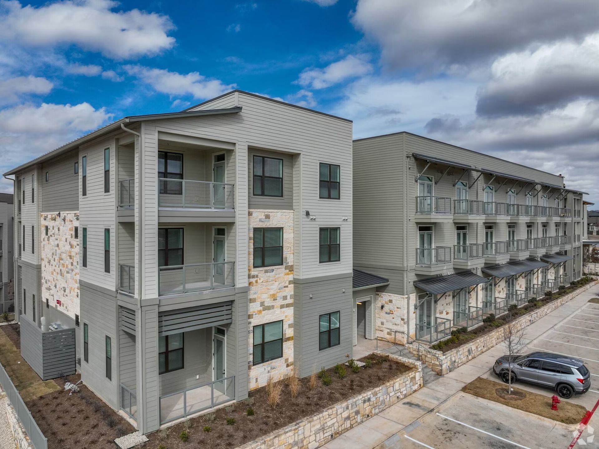 Apartment complex with gray siding and balconies under a cloudy blue sky