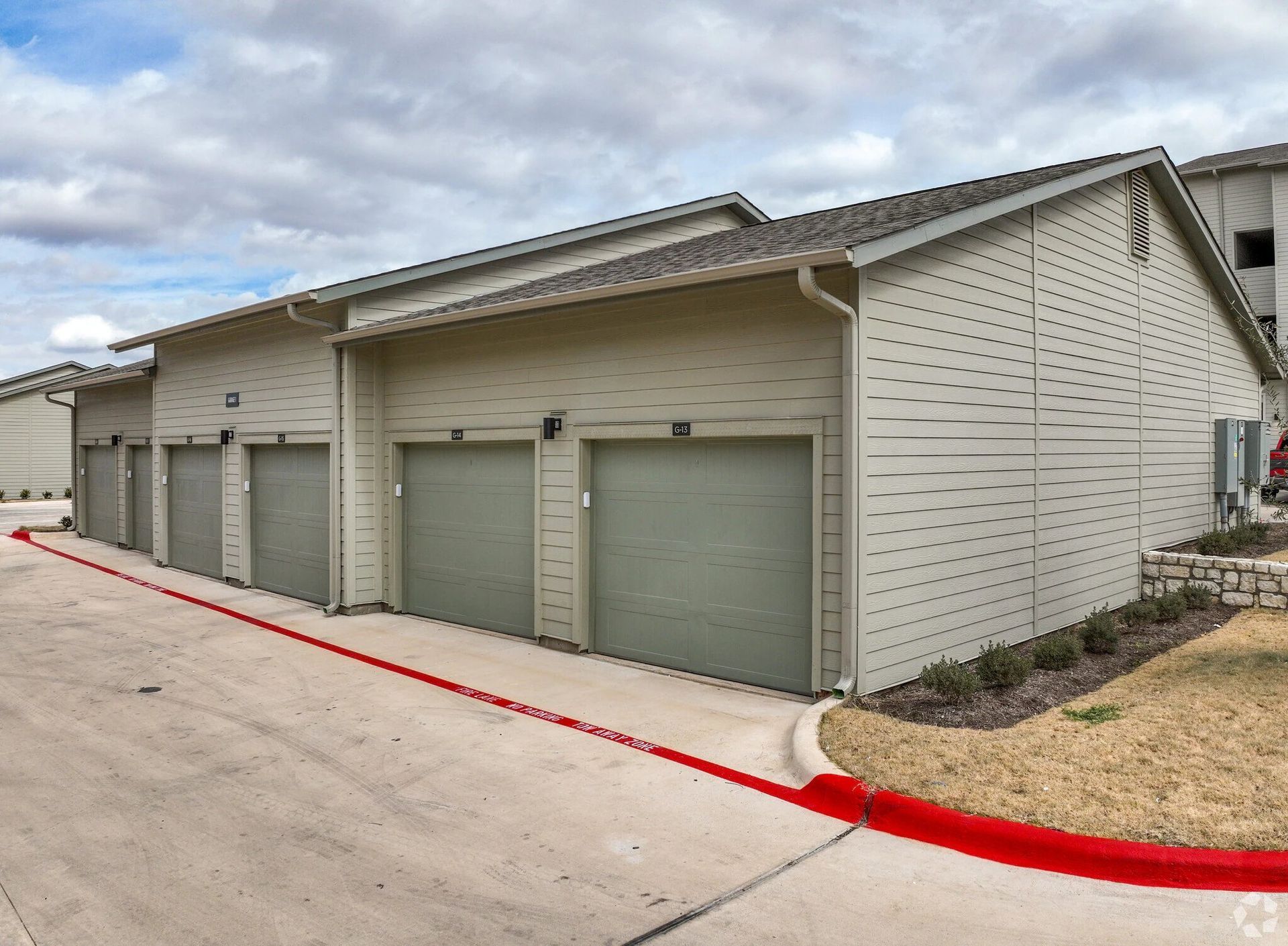 Row of beige garage units along a curved red curb in a residential complex