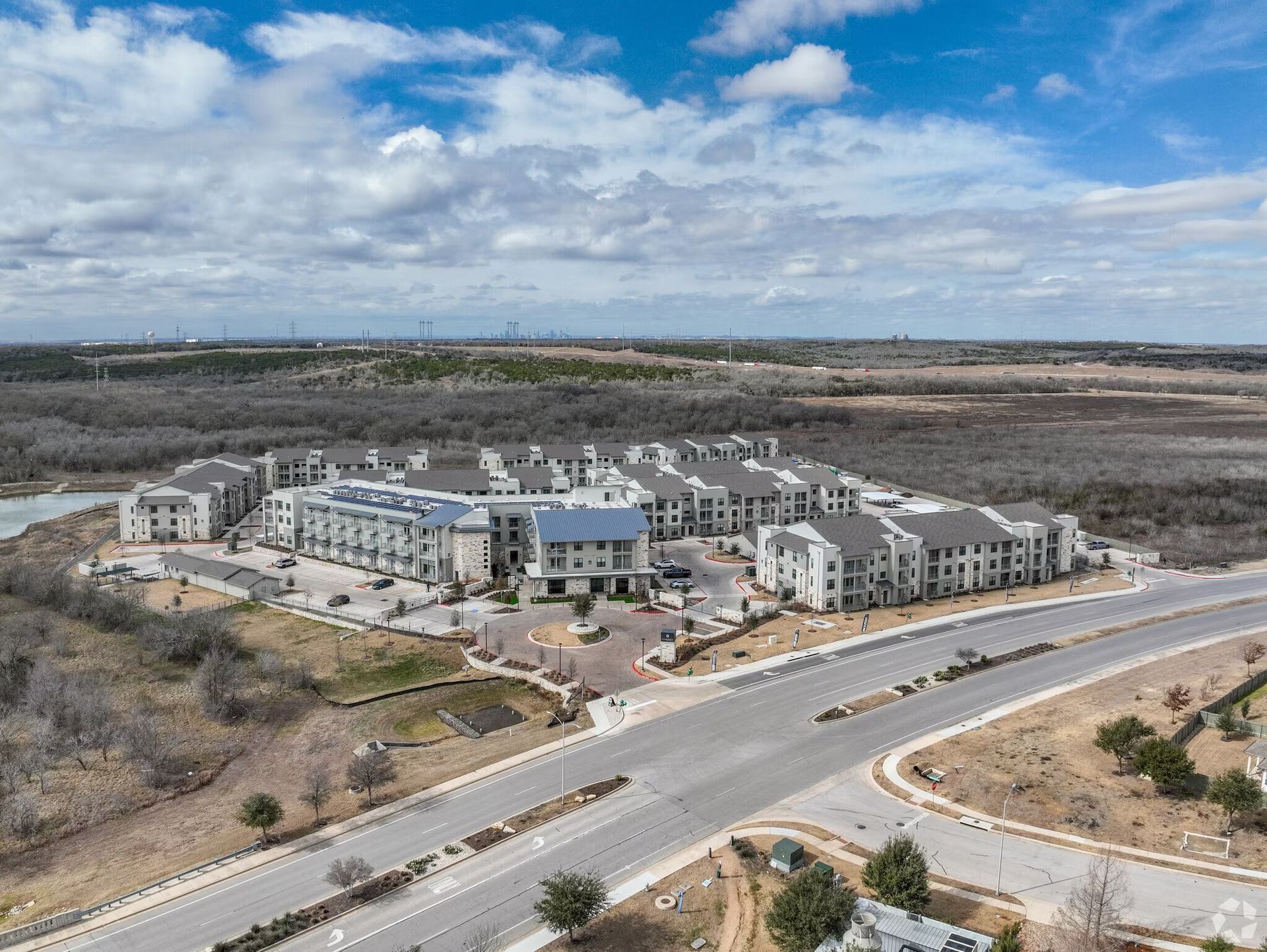 Aerial view of a modern apartment complex beside a curving road under a cloudy sky