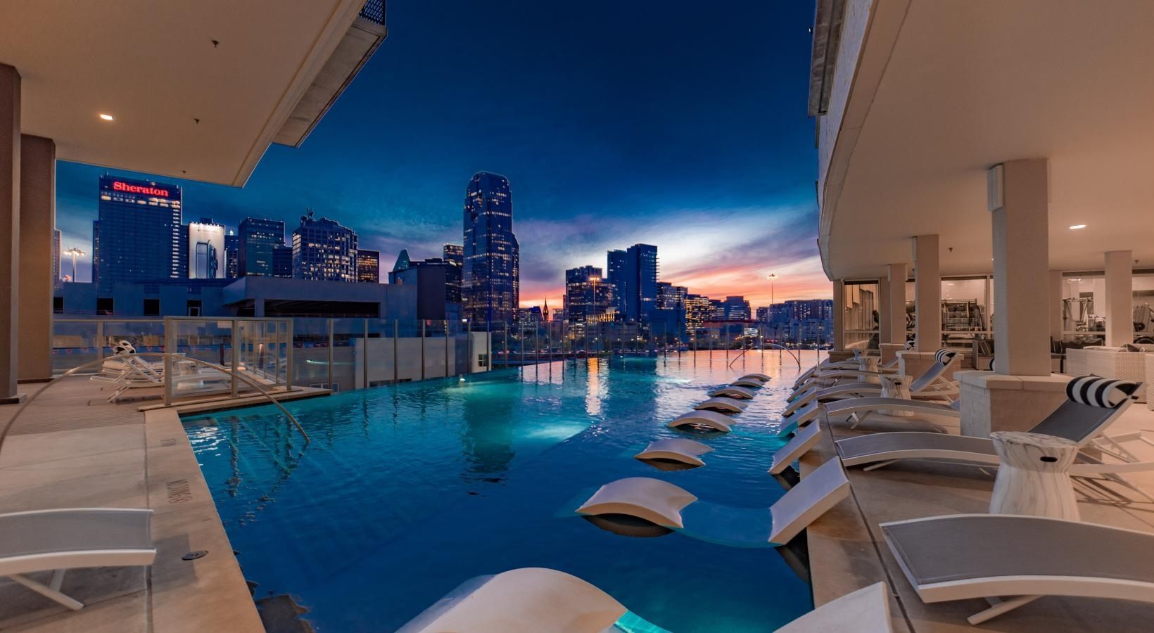 Luxury rooftop infinity pool at dusk with city skyline reflections and lounge chairs