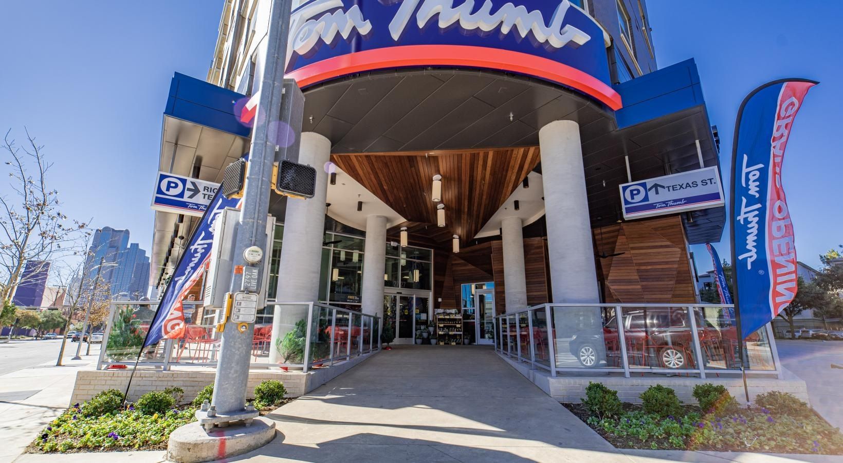 Entrance to a building with a red and blue awning, glass doors, and outdoor flags on a sunny day