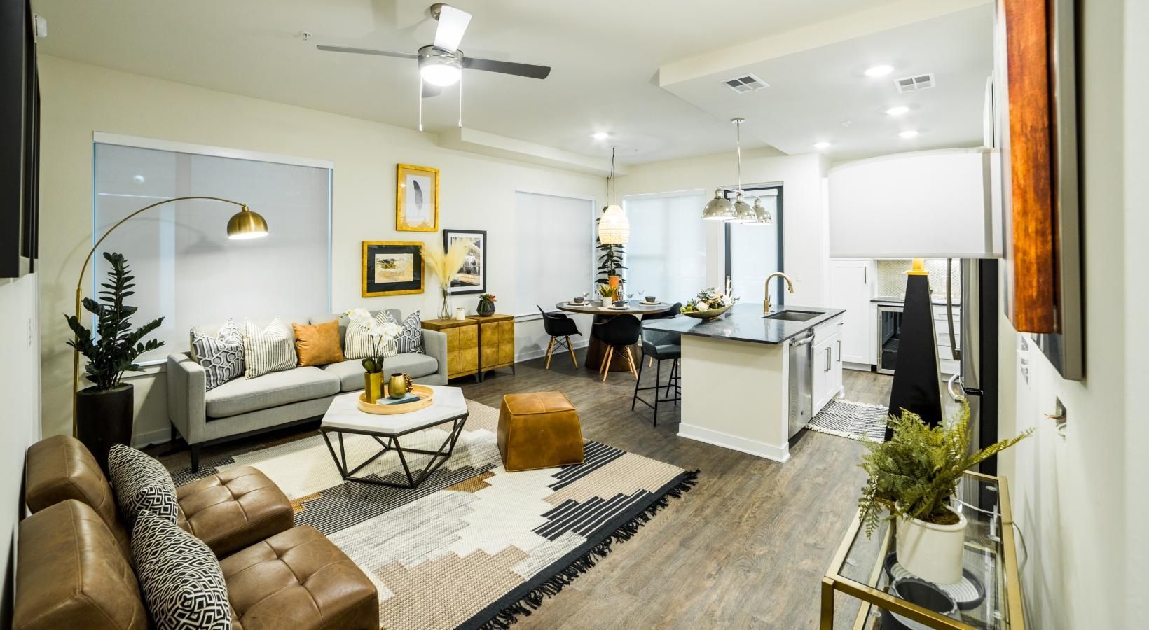 Bright living room with beige sofa, patterned rug, white kitchen island, and ceiling fans