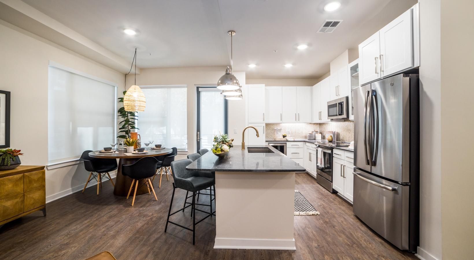 Bright modern kitchen and dining area with white cabinets, island, stainless fridge, and dark wood floors.