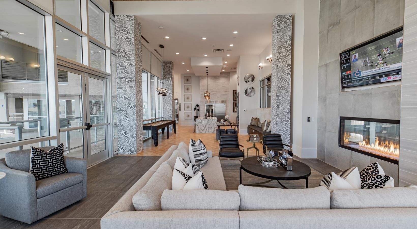 Modern hotel lobby with beige sofas, glass walls, fireplace, and a long hallway seating area