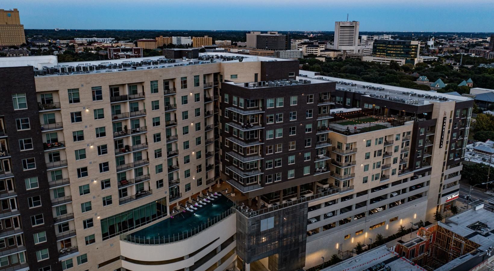 Aerial view of a modern apartment complex with a rooftop pool at dusk.