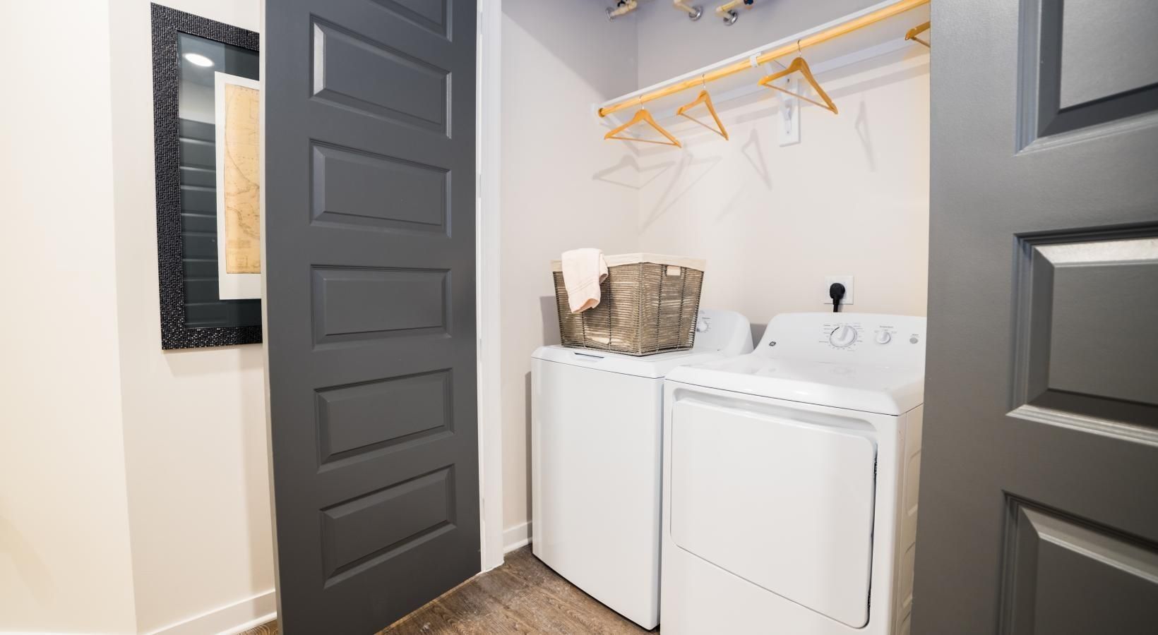 Laundry closet with stacked washer and dryer, gray doors, and hanging shelves with a basket on top