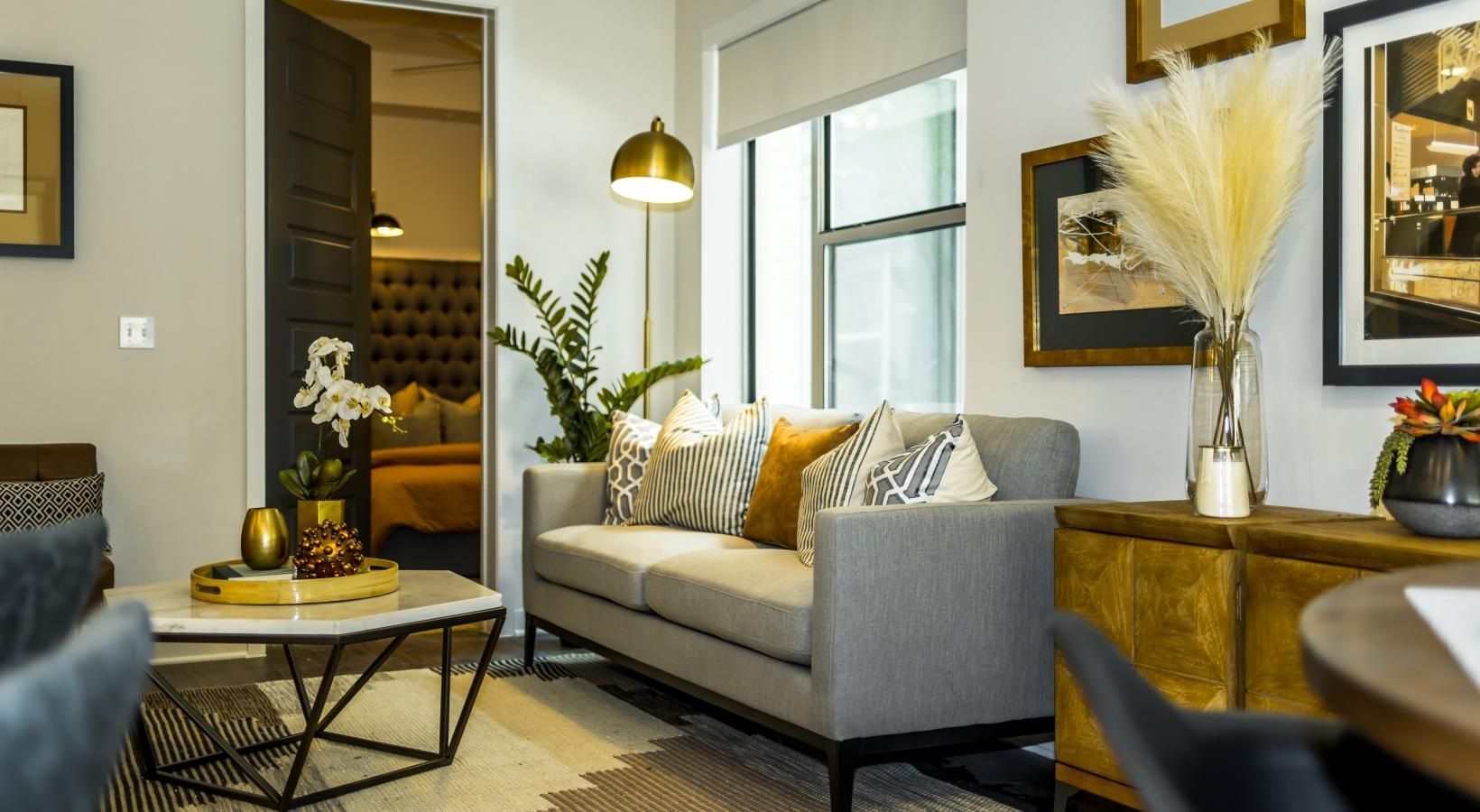 Modern living room with gray sofa, gold accents, black coffee table, and warm decor by a window