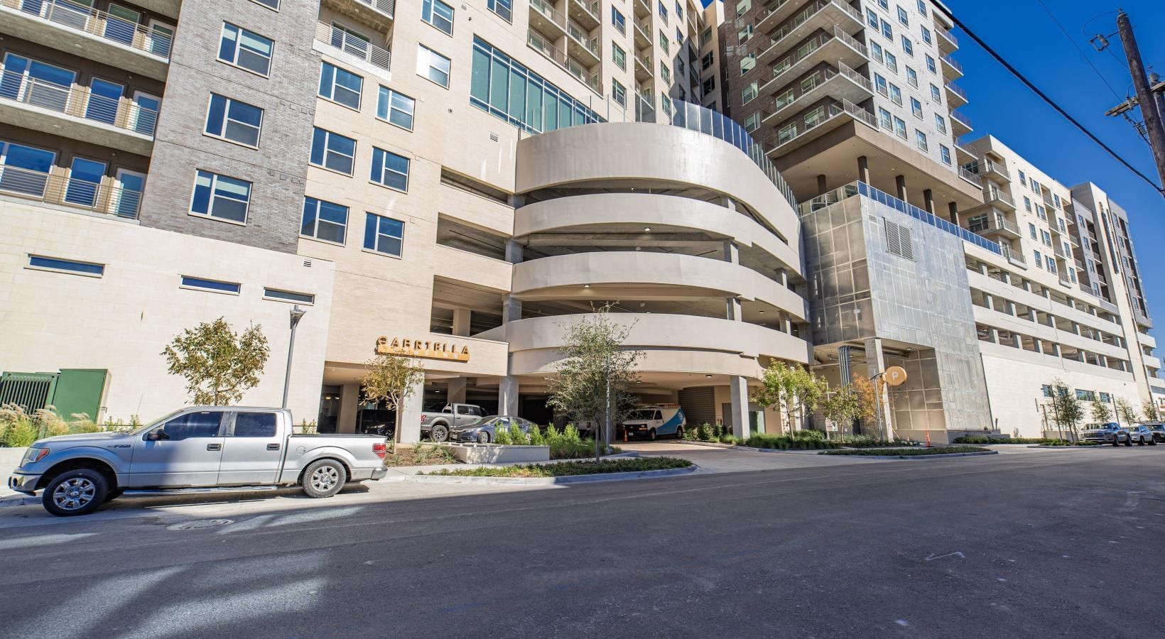 Hotel entrance with parked silver pickup, white multi-story building, and curved awning on a sunny street