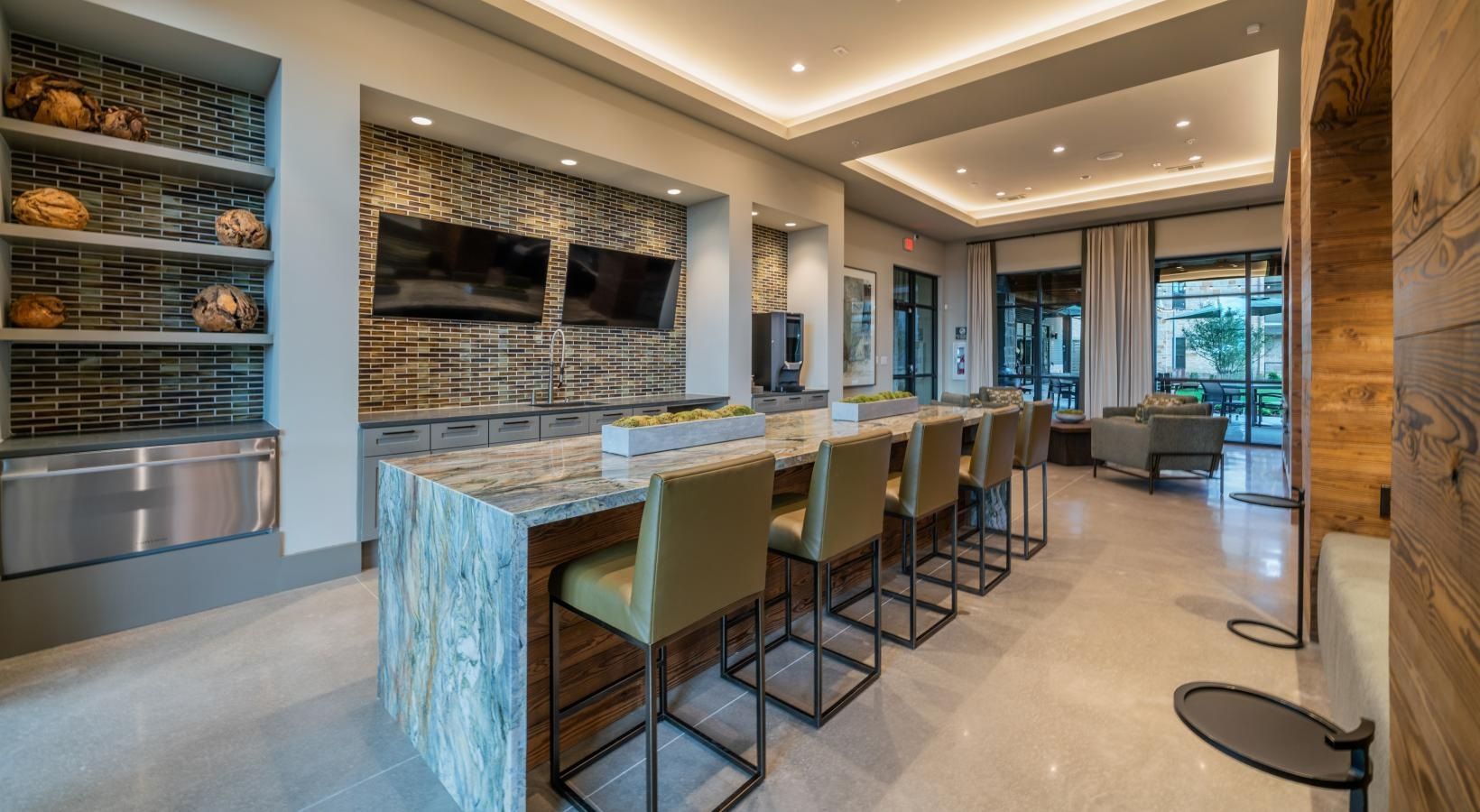 Modern kitchen with marble island, bar stools, built-in TV, and floor-to-ceiling windows overlooking a patio