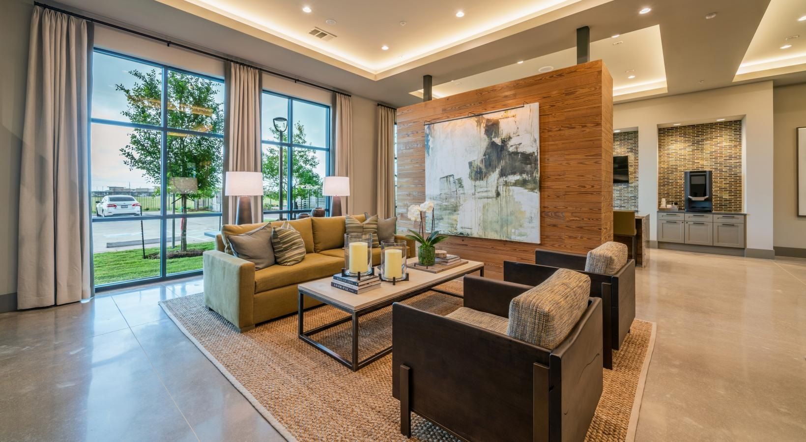Modern living room with beige sofas, glass coffee tables, large windows, and wood-paneled accent wall.