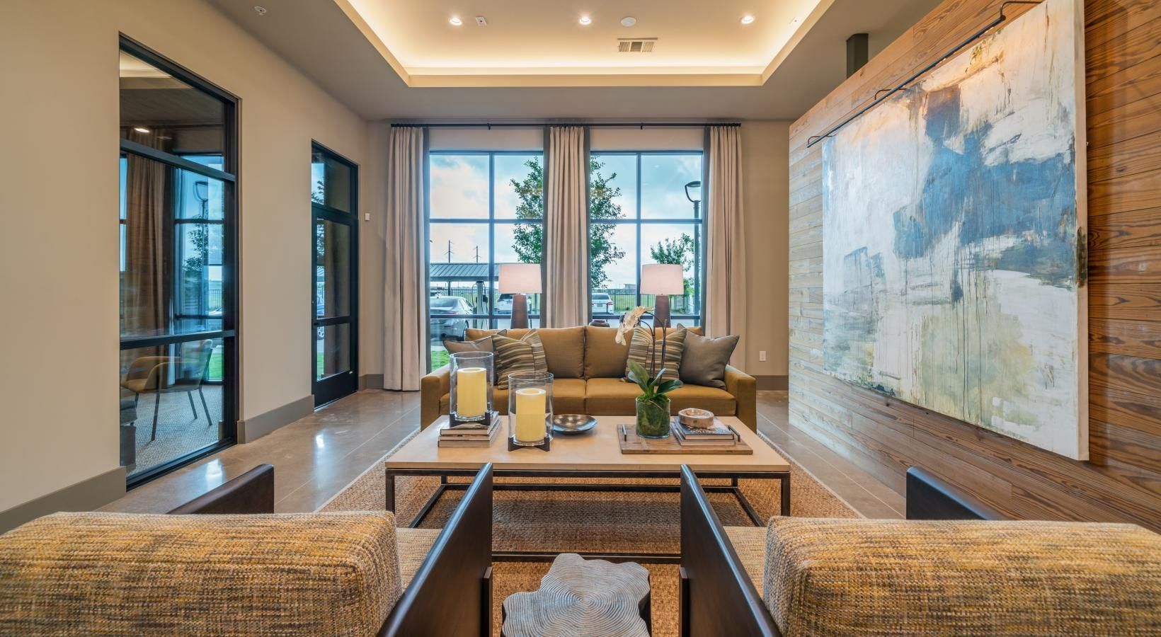 Modern hotel lobby with beige sofas, a coffee table, and large abstract wall art near windows.