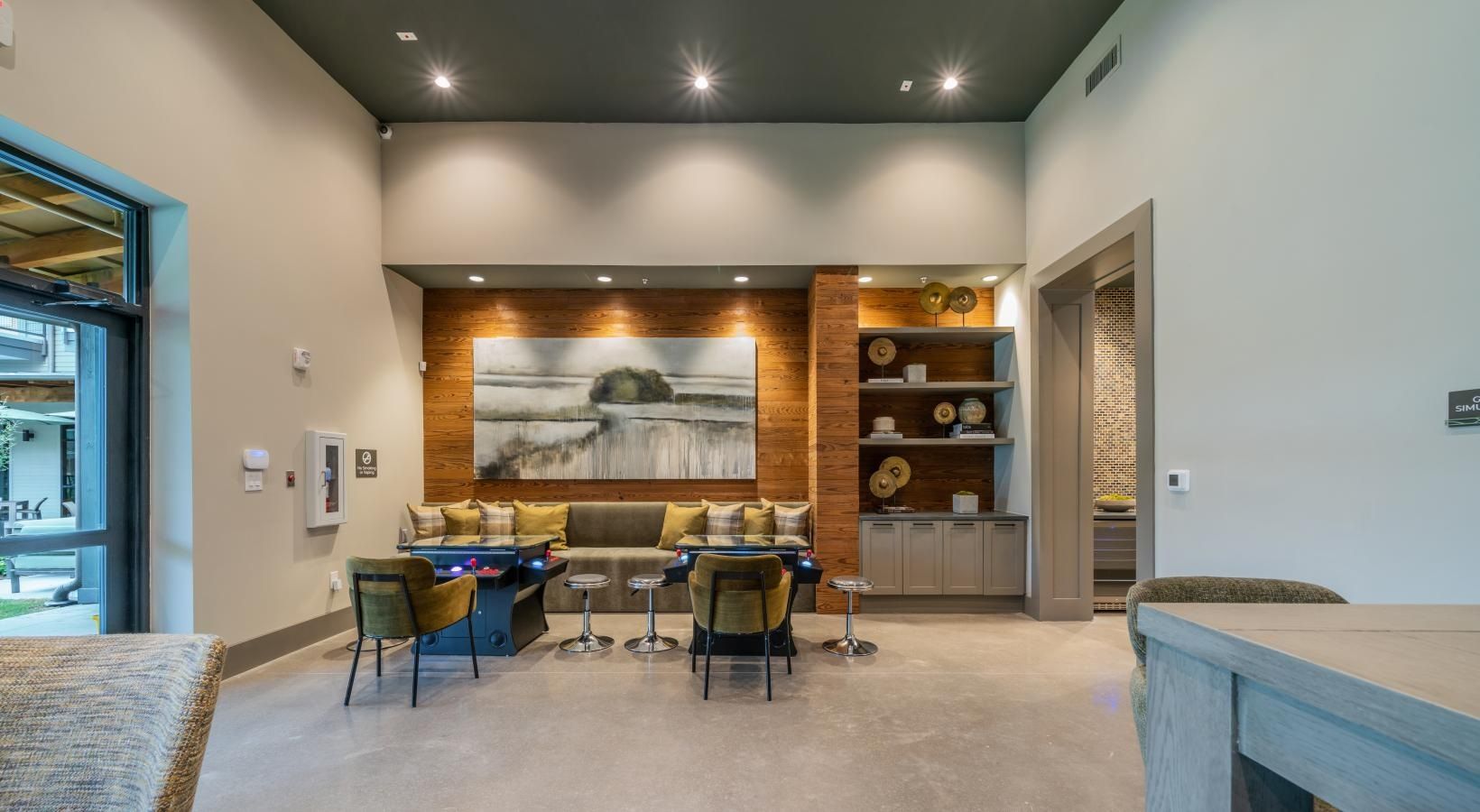Modern waiting area with gray couches, wood accent wall, and dining table under recessed lights