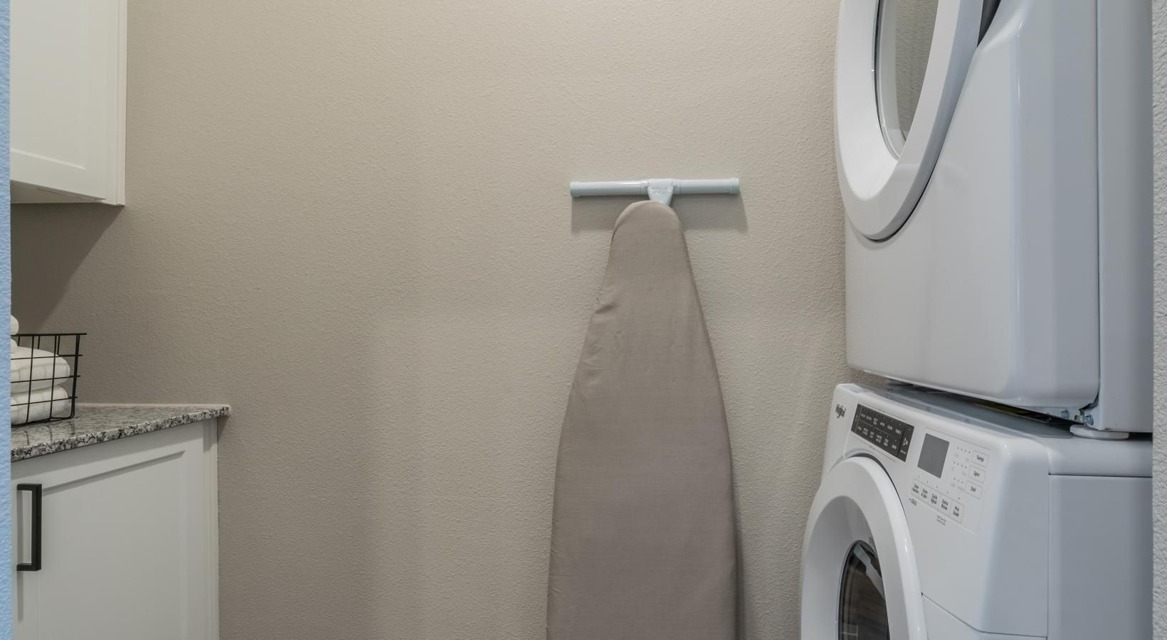 Laundry room with stacked washer and dryer beside a wall-mounted ironing board.