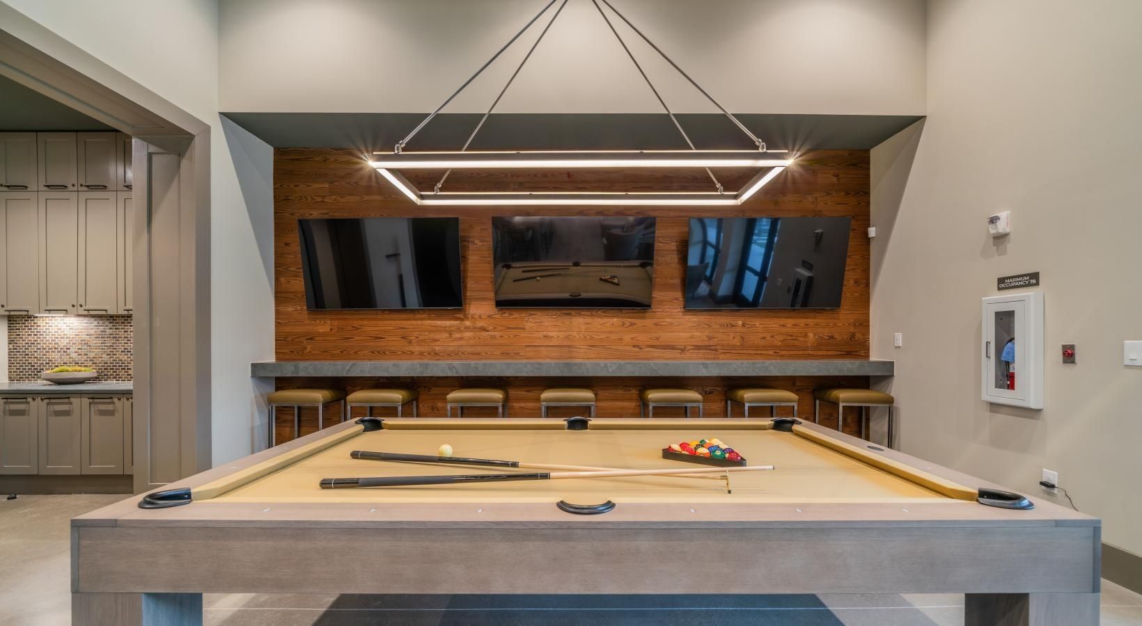 Modern game room with a pool table beneath pendant lights and wall-mounted TVs.
