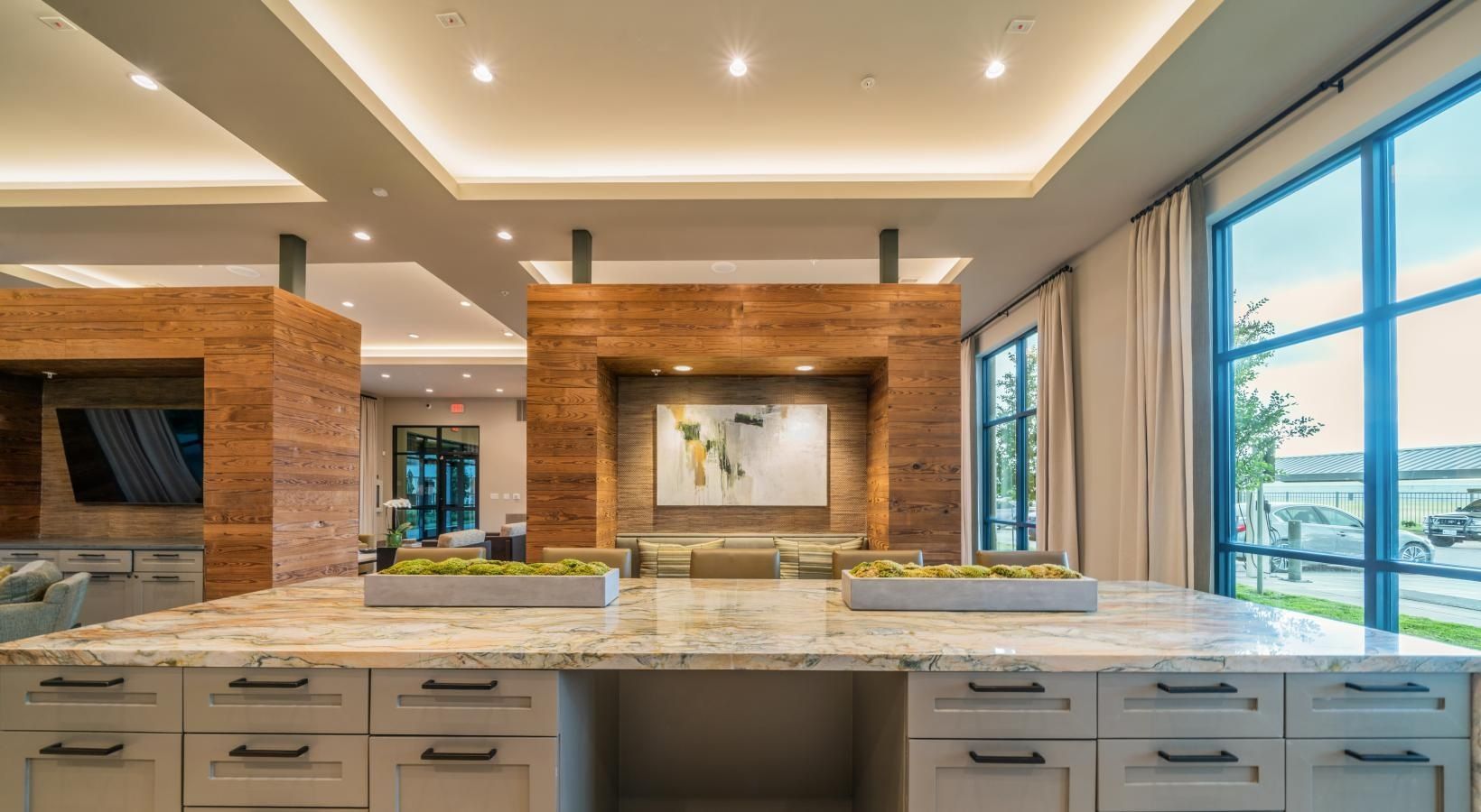 Modern kitchen with a large marble island, warm wood accents, and floor-to-ceiling windows overlooking a balcony.