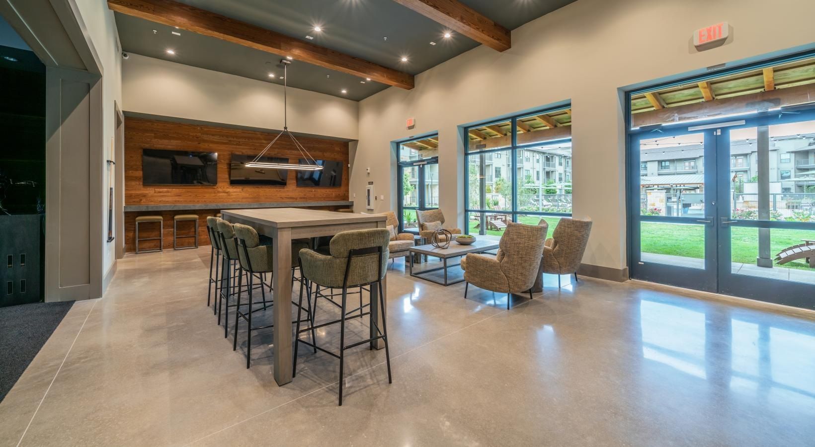 Modern lobby with high ceilings, bar stools, lounge chairs, and large windows overlooking greenery