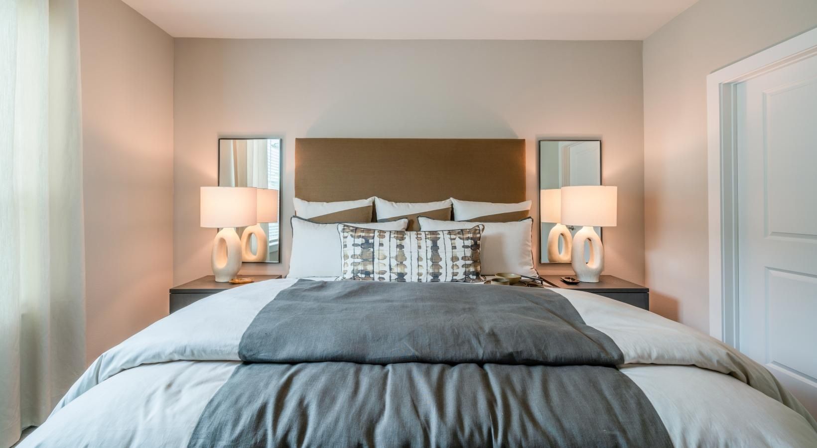 Bright modern bedroom with a made bed, gray bedding, white pillows, and matching bedside lamps.