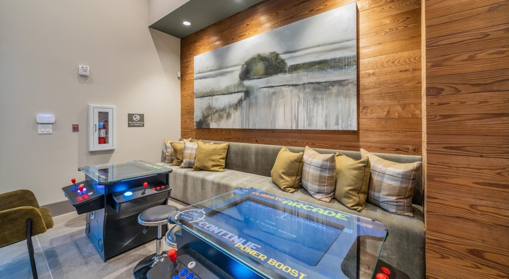 Modern lobby seating area with tan couches, glass tables, and a large landscape painting on wood paneling