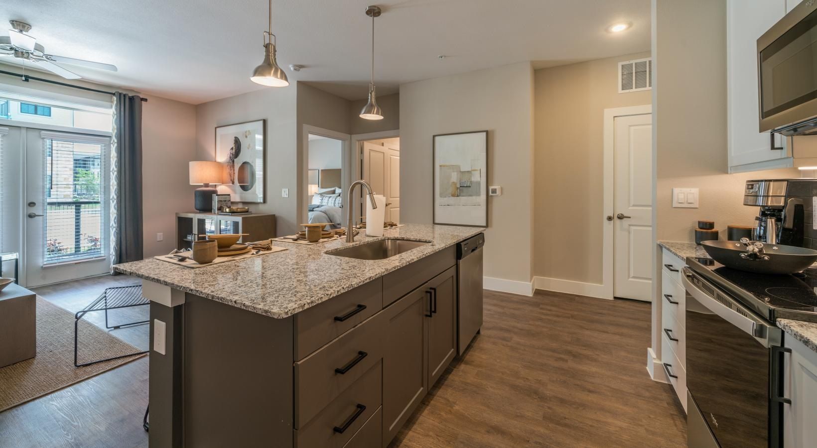 Modern kitchen with island, granite countertops, pendant lights, and adjoining living area