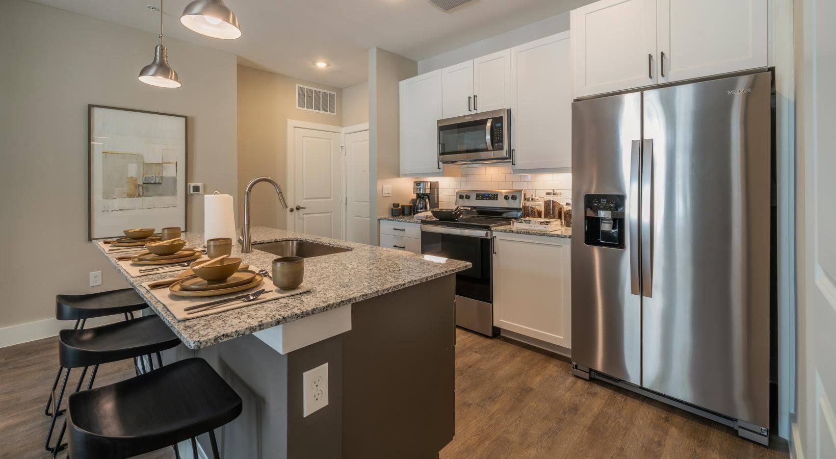 Modern kitchen with stainless steel appliances, granite island, and two black stools set for dining