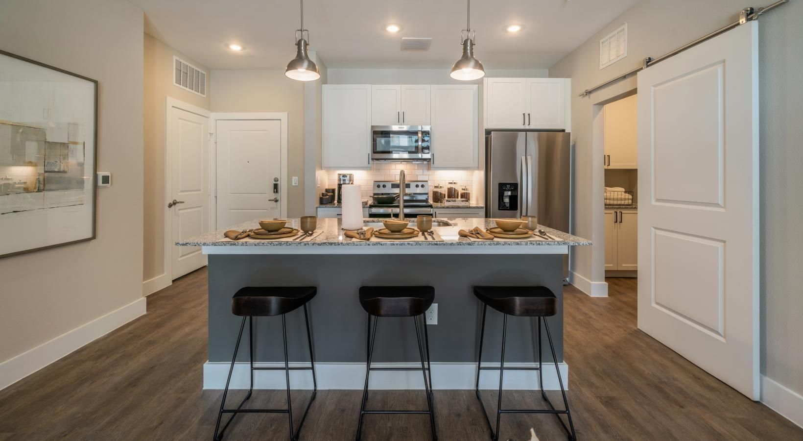 Modern kitchen with white cabinets, stainless appliances, island, and three black stools