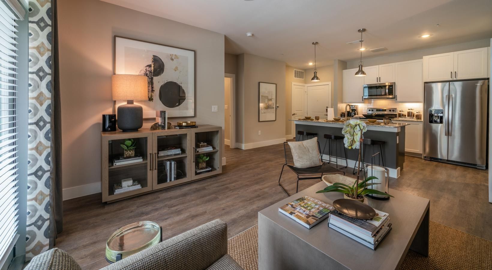 Open-plan living room and kitchen with gray furniture, wood floors, and stainless-steel appliances
