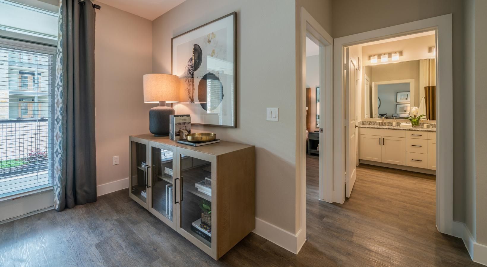 Hallway with console table and lamp, leading to a bright bathroom through an open doorway