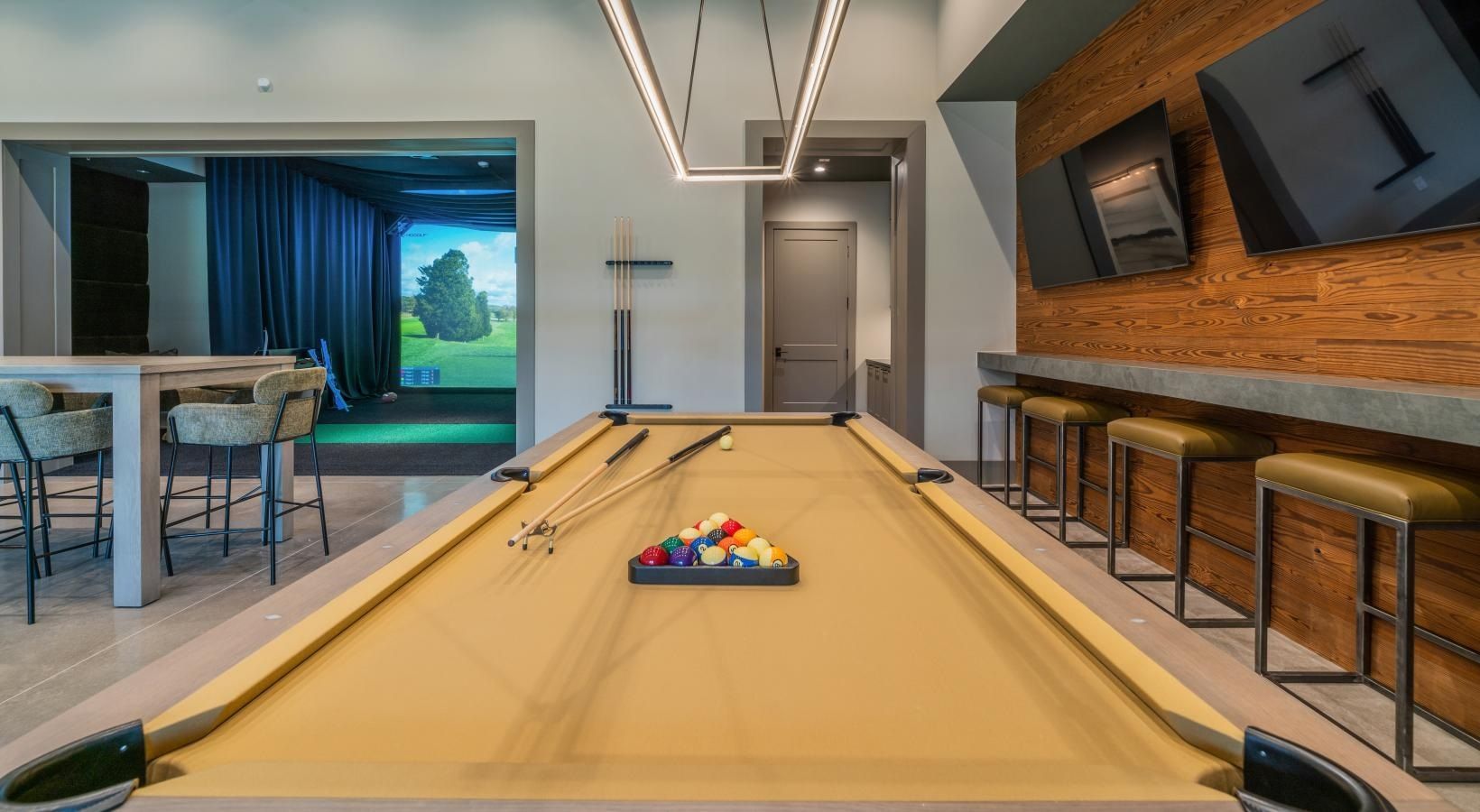 Modern game room with a pool table, wall-mounted TVs, bar stools, and sliding doors to a patio