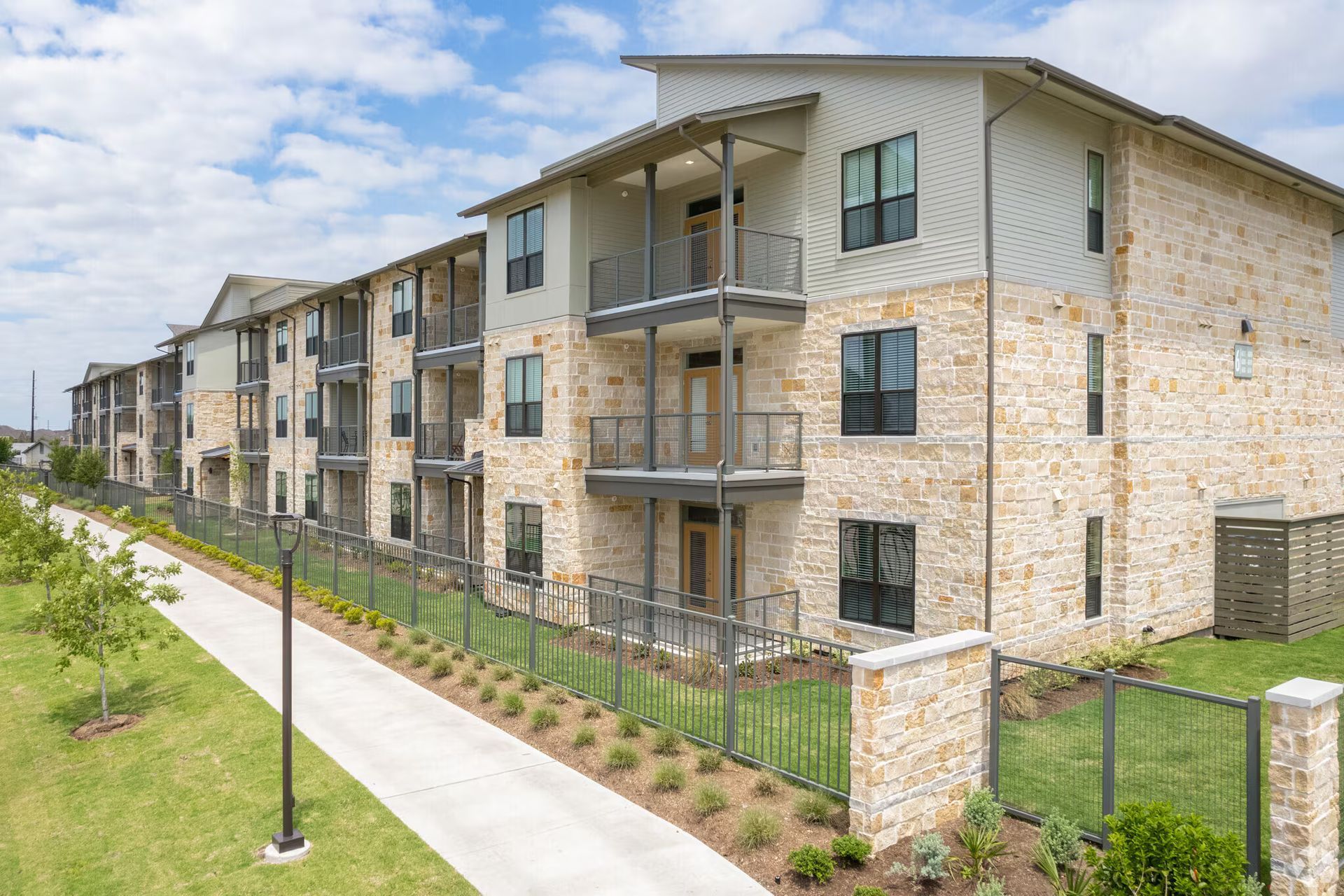 Modern apartment complex with balconies, stone siding, and a sidewalk beside a grassy lawn