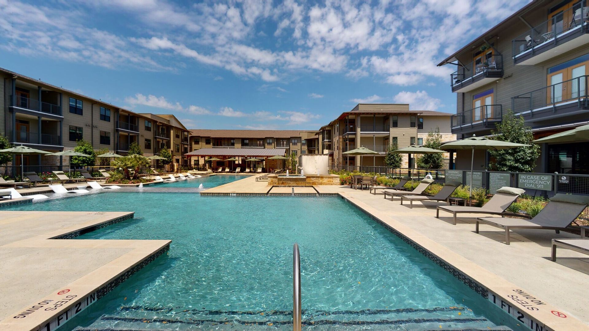 Modern apartment courtyard with a turquoise swimming pool and lounge chairs under a blue sky