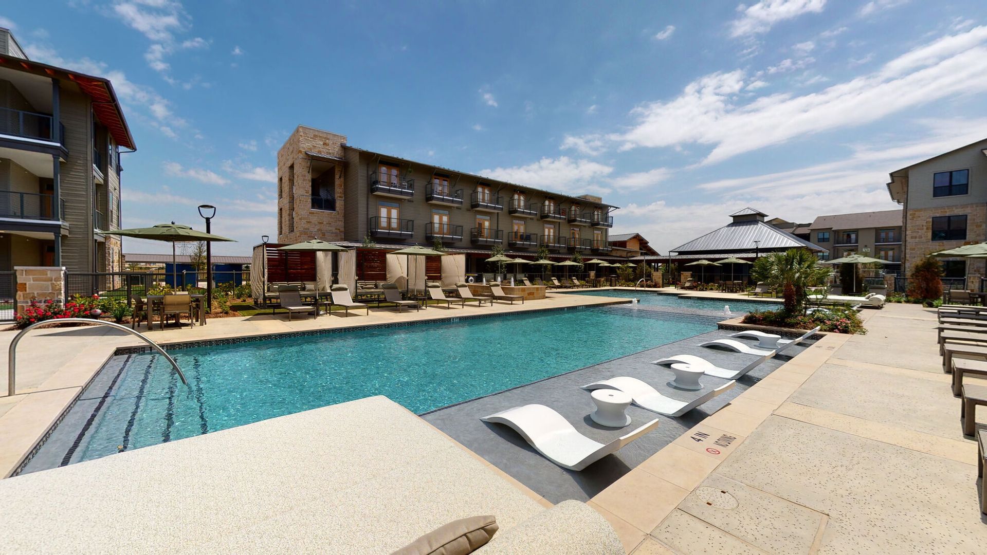 Outdoor pool with lounge chairs beside a modern hotel complex on a sunny day