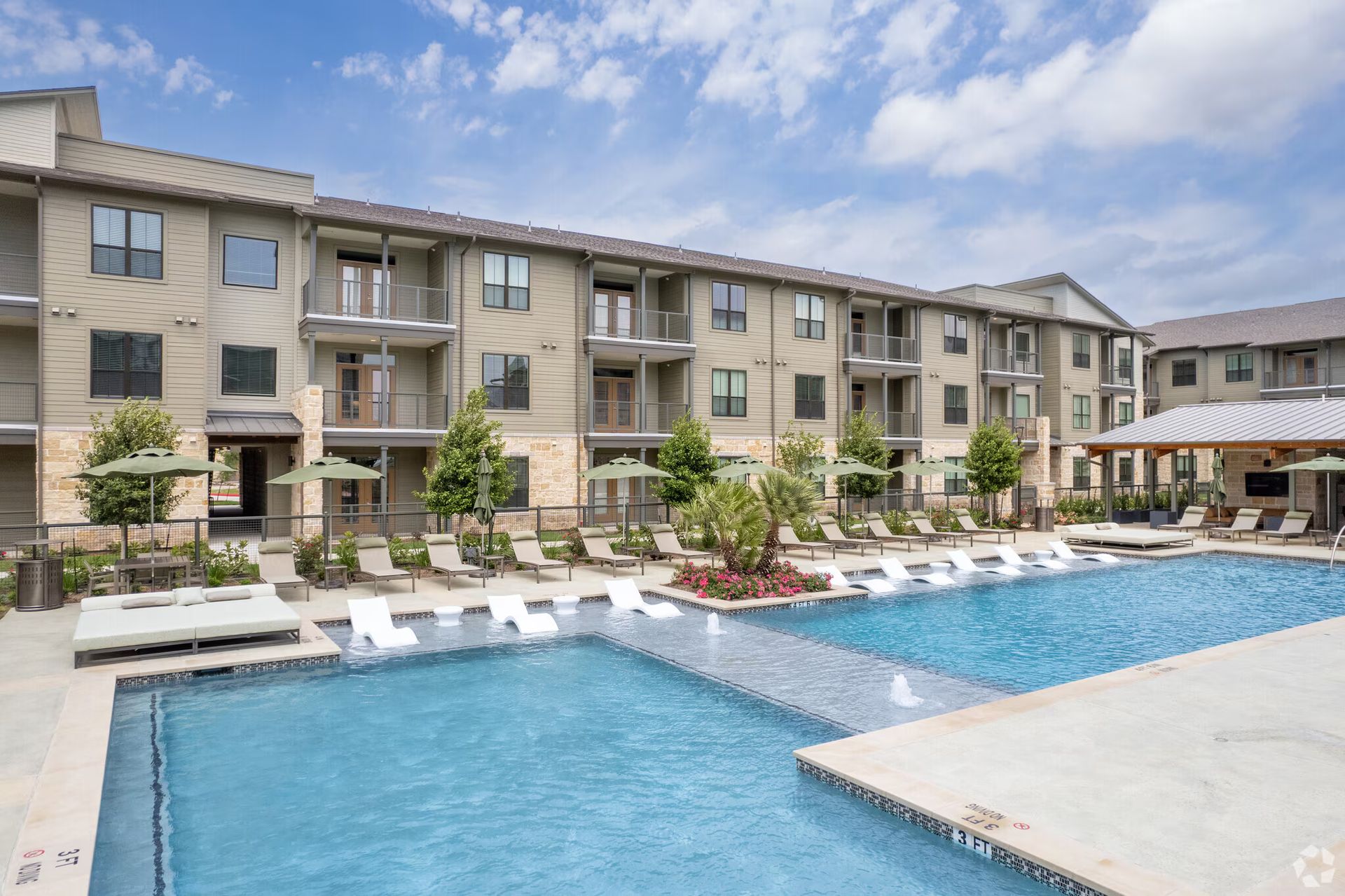 Apartment complex with a blue swimming pool and lounge chairs under a partly cloudy sky