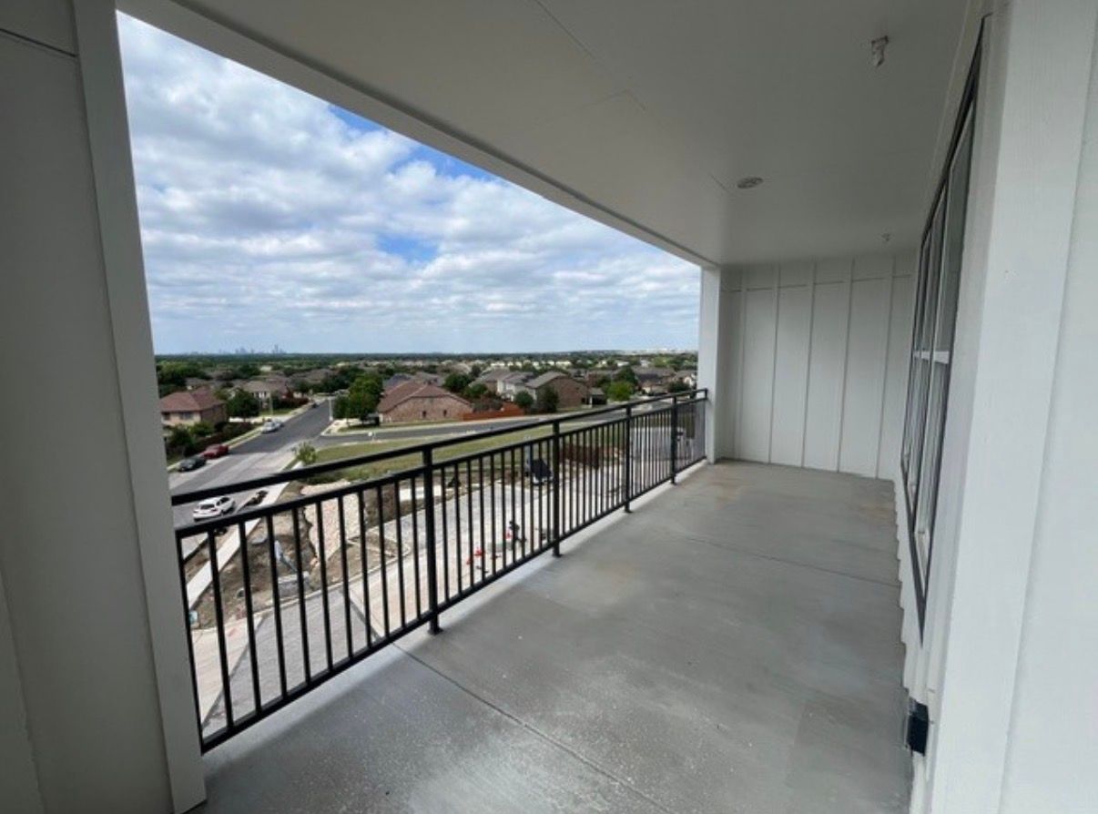 Empty covered balcony with black railing overlooking a neighborhood and cloudy sky