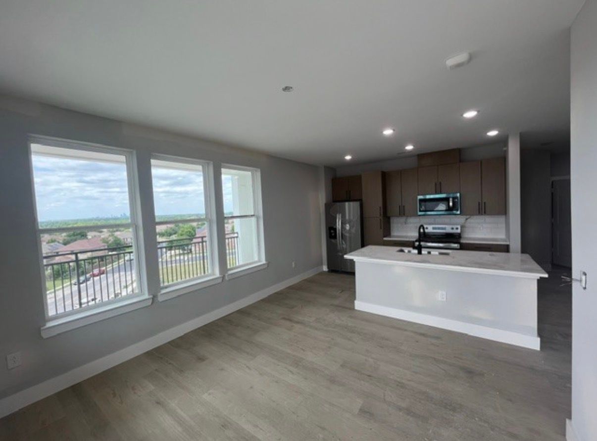 Empty modern kitchen and living area with gray walls, white island, and large windows overlooking a balcony.