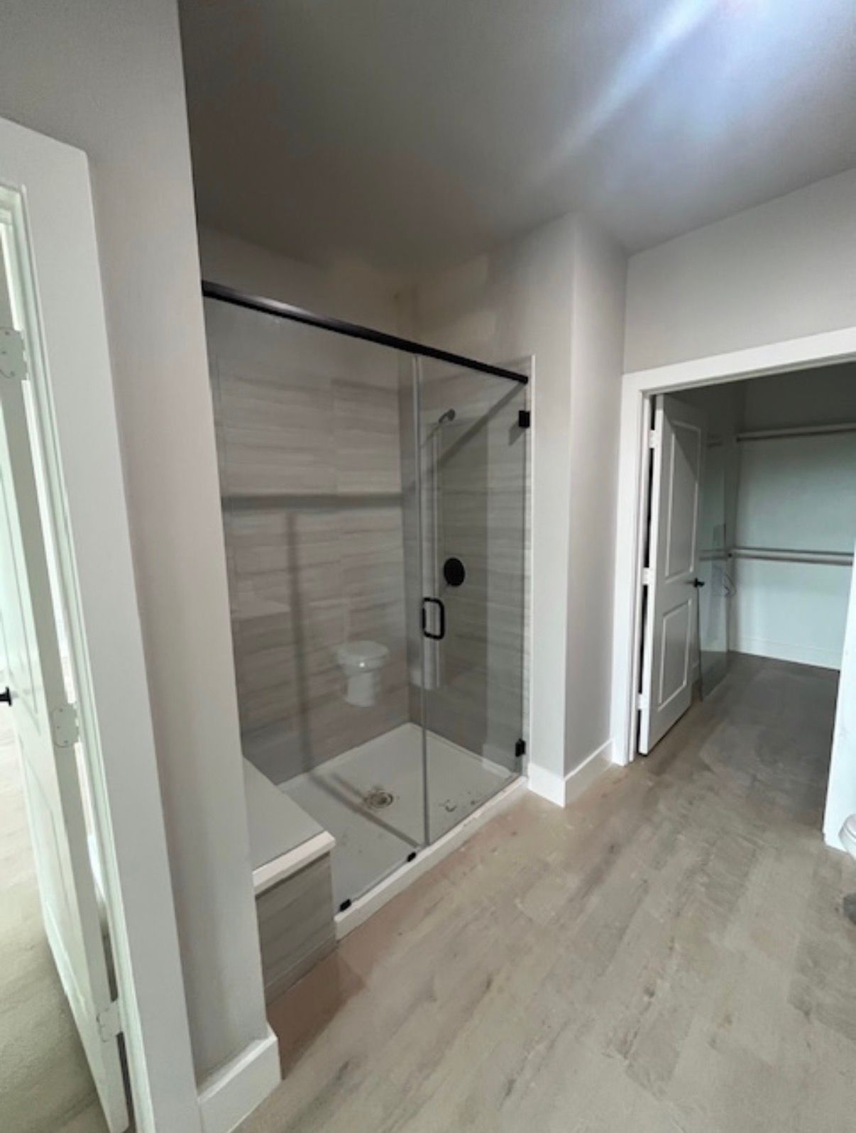 Empty modern hallway with glass shower enclosure on the left and open closet doorway ahead
