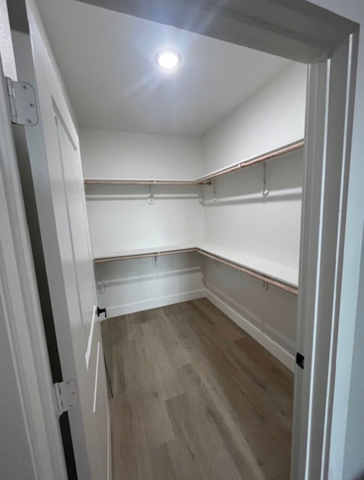 Empty walk-in closet with white walls, built-in shelves, and wood flooring, viewed from the doorway.