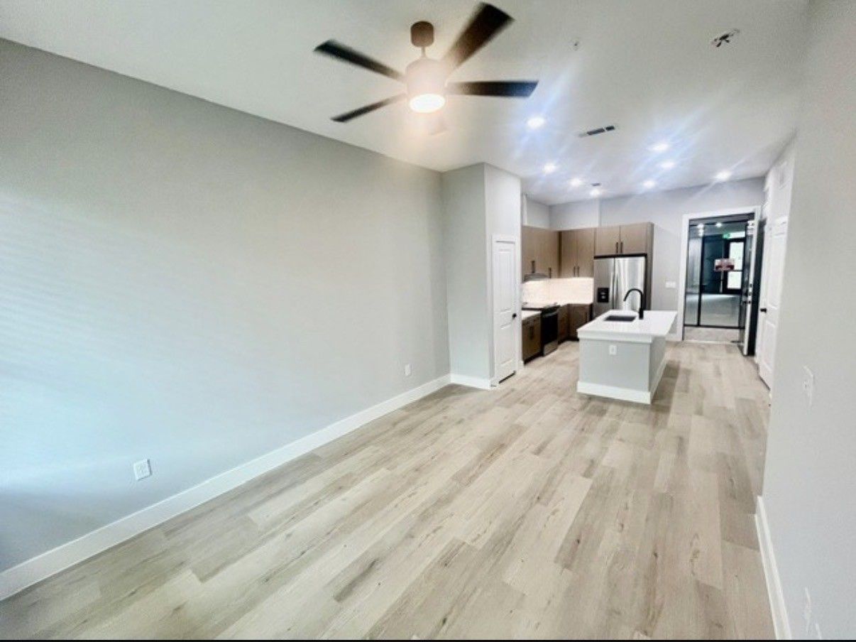 Open-concept living room and kitchen with light wood floors, white walls, and ceiling fan.