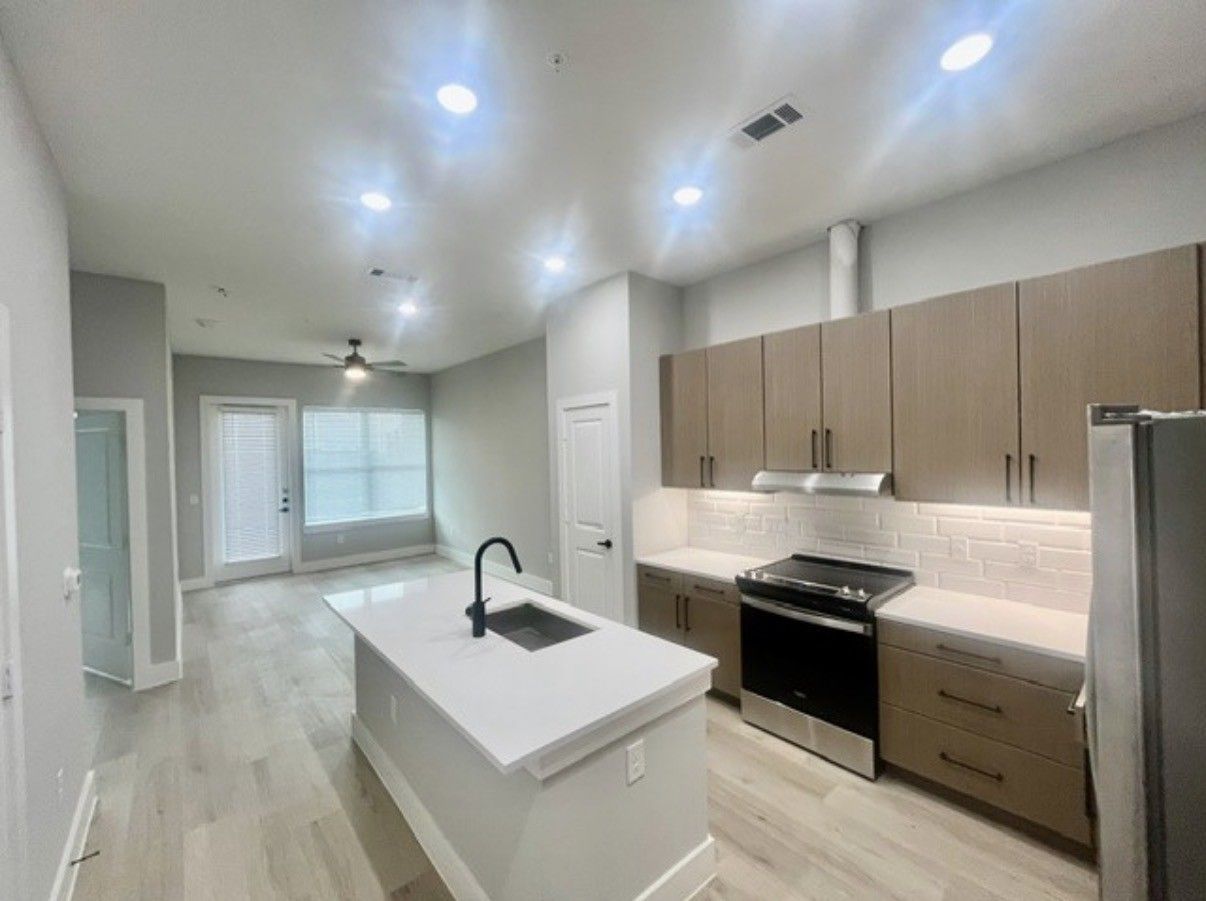 Modern white kitchen with island, wood cabinets, stainless appliances, and bright recessed lighting