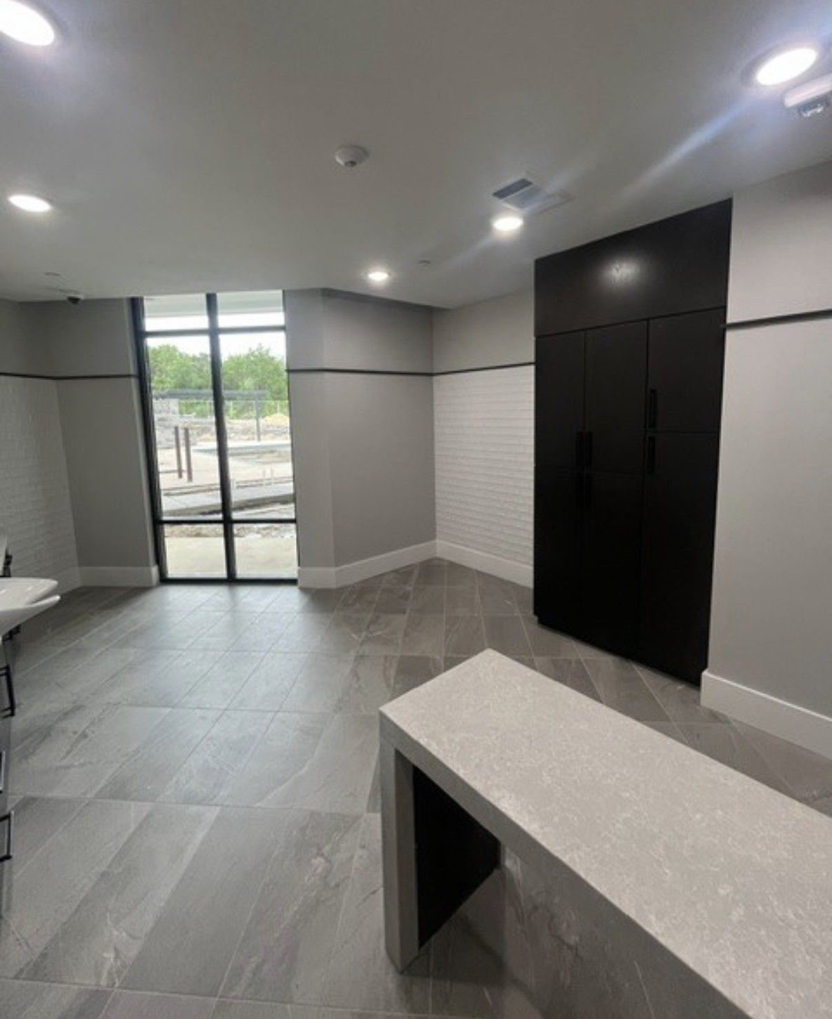 Modern empty room with gray tile floor, black built-in cabinets, and a glass door to outside.