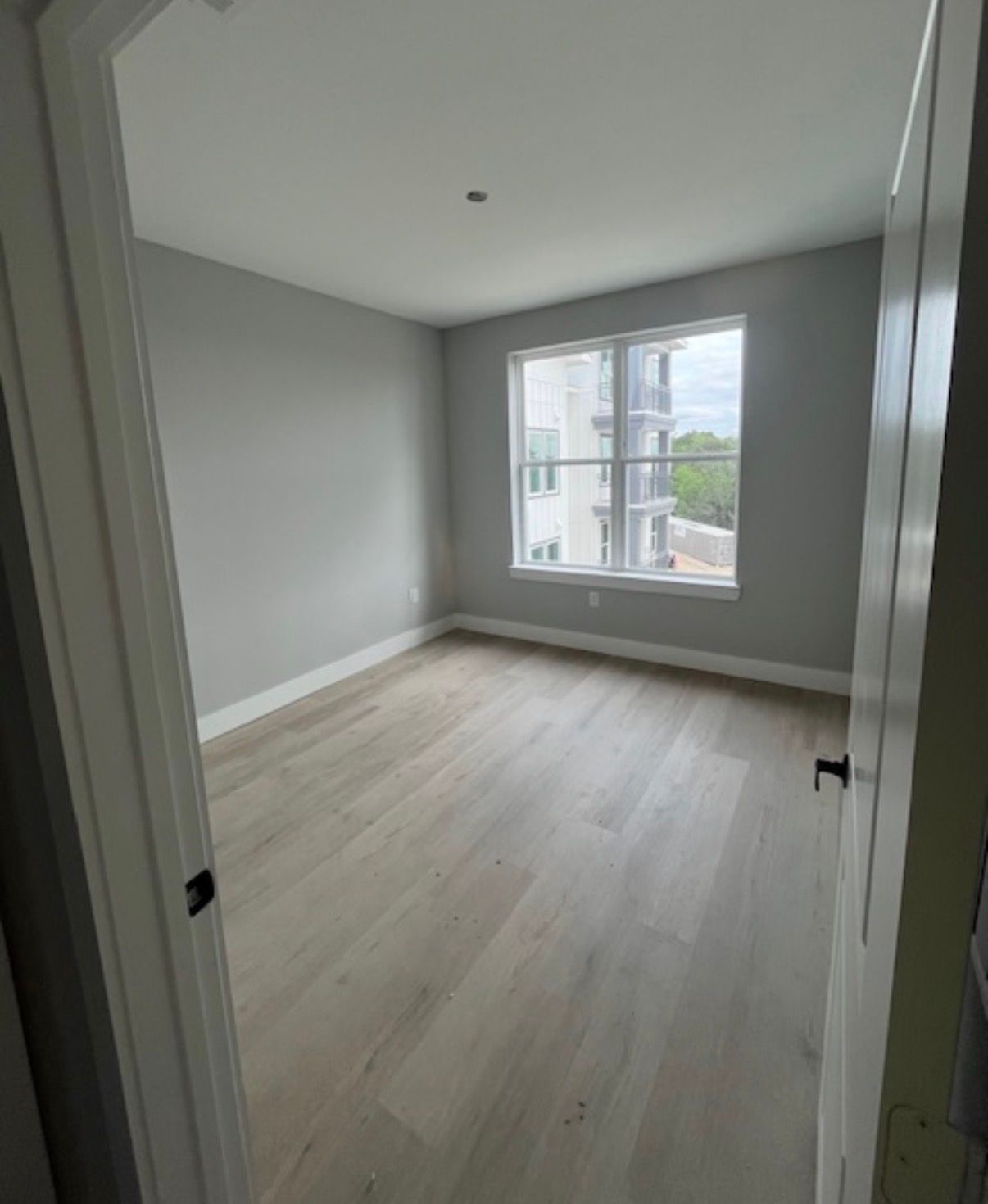 Empty gray bedroom with light wood floor and a window