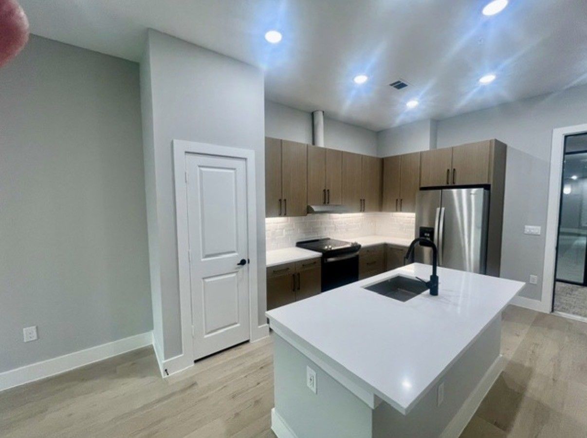 Modern kitchen with white island, light wood cabinets, stainless steel fridge, and recessed ceiling lights