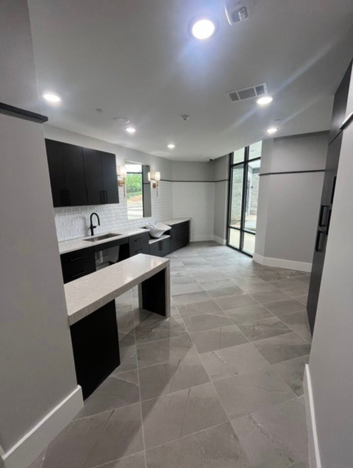 Modern gray kitchen with black cabinets, white island, tiled floor, and sliding glass doors to a patio