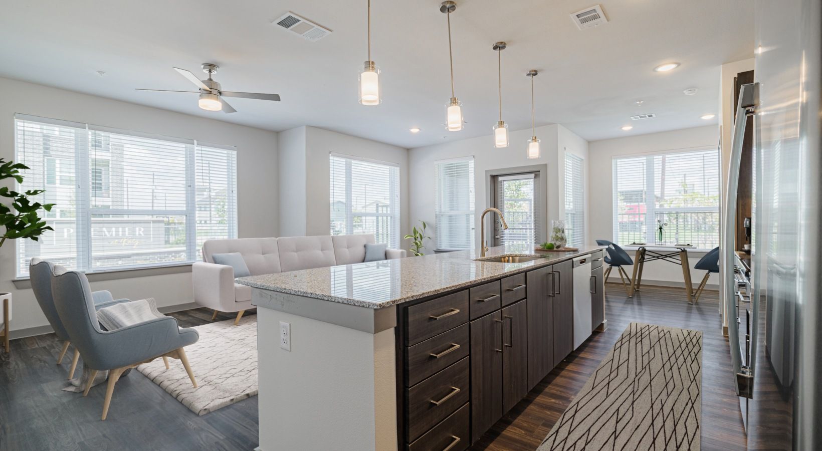Bright modern open-plan living room and kitchen with white sofas, island, pendant lights, and large windows