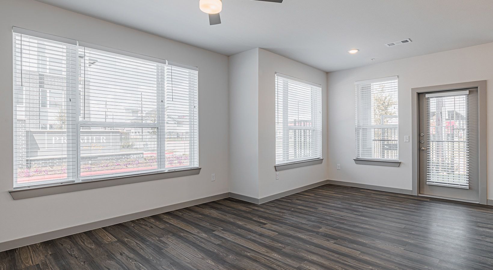 Bright empty room with large windows, gray walls, dark wood floors, and a glass door