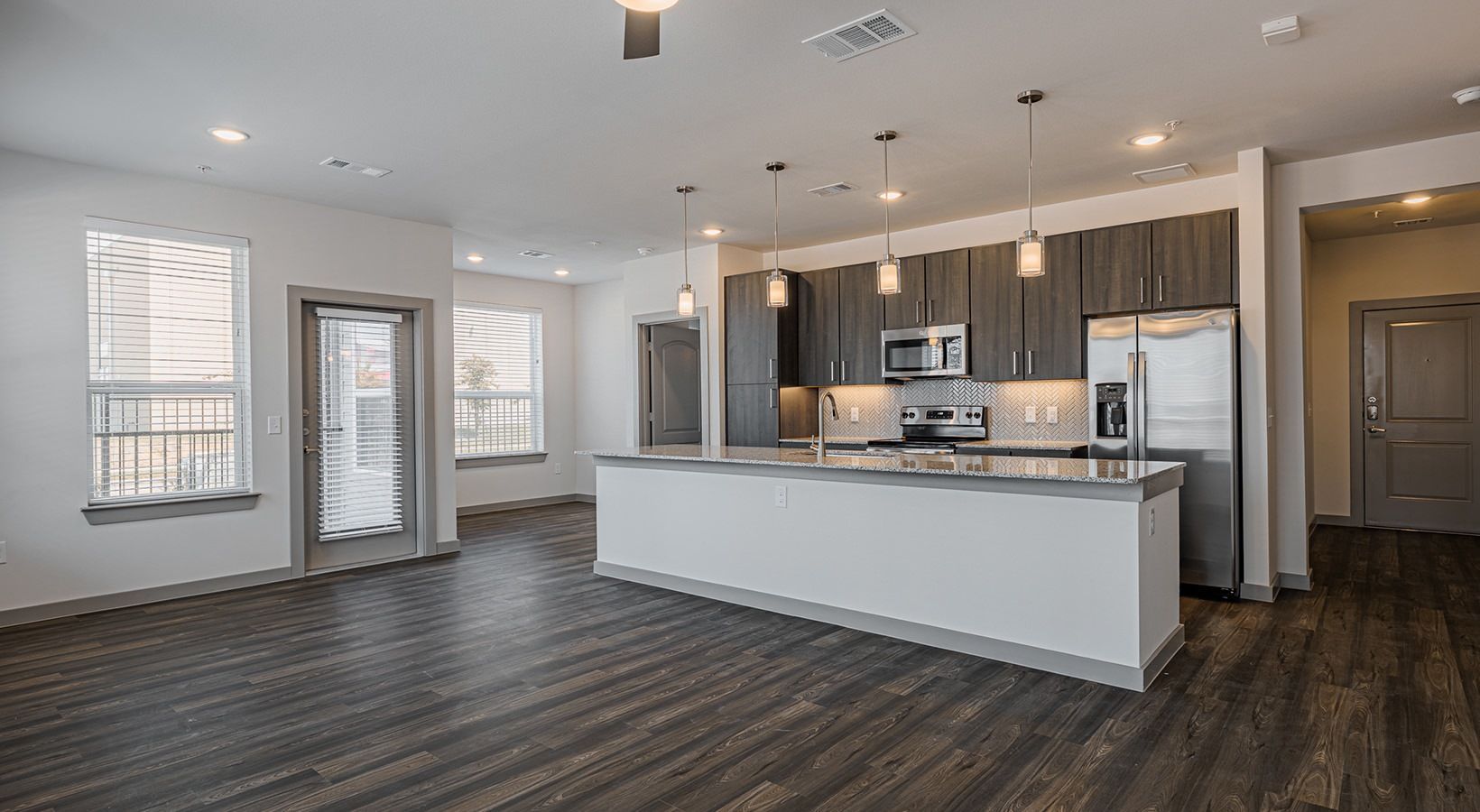 Modern open-concept kitchen and living area with gray cabinets, white island, stainless appliances, and dark floors