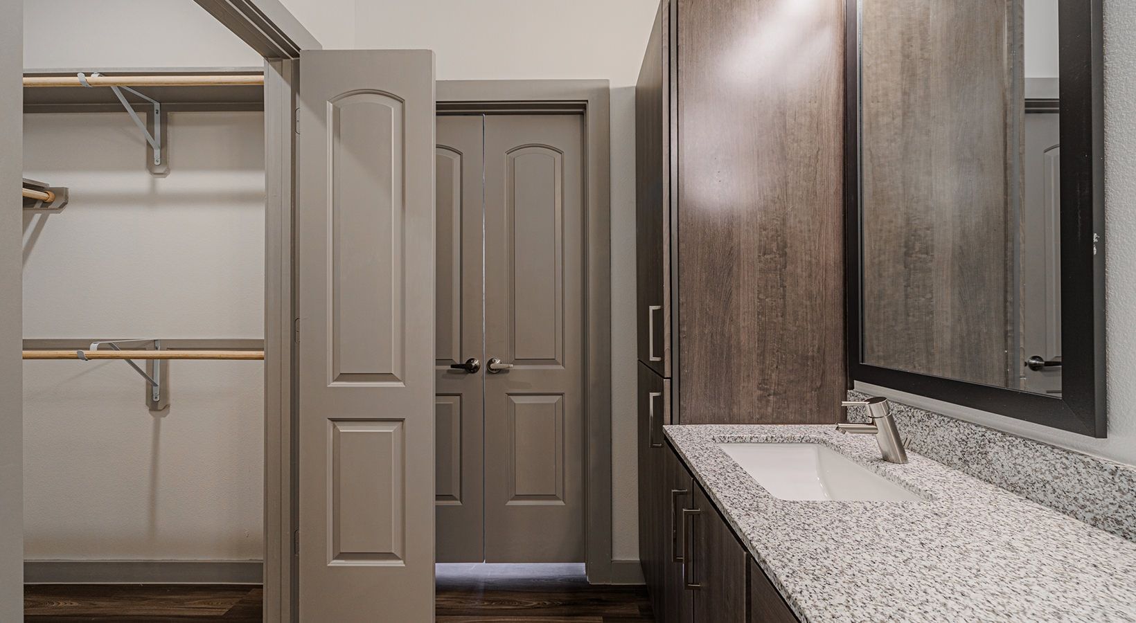 Luxury bathroom vanity with granite countertop and large mirror, beside an open closet and closed door