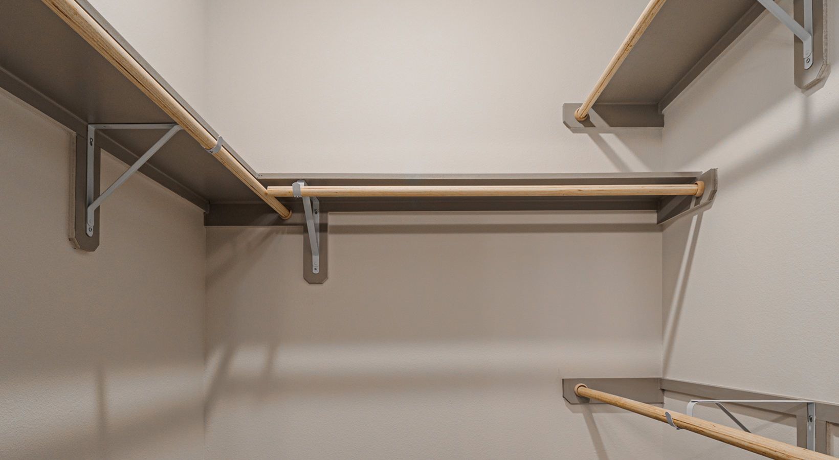 Empty walk-in closet with white walls, wood shelves, and hanging rods on both sides.