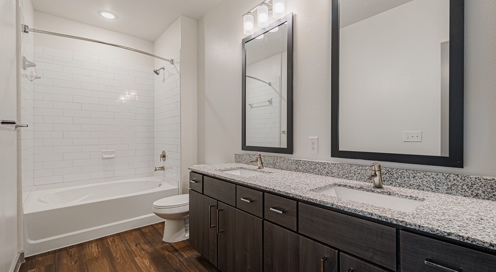 Modern bathroom with double vanity, large mirrors, and a tiled shower-tub combo.