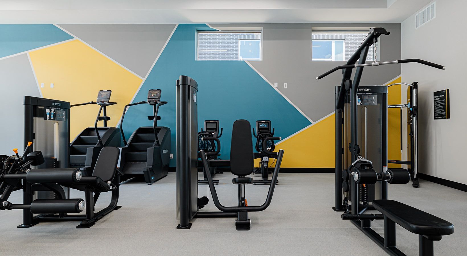 Modern gym with weight machines and equipment against a gray wall with yellow and blue geometric accents